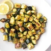 Roasted zucchini cubes on a white plate with a slice of lemon on the side. An option as side dishes for tilapia.