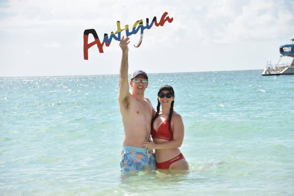 couple standing in  the ocean holding a sign that says Antigua