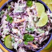 Colorful slaw with purple cabbage and herbs in a blue bowl with lime slices.