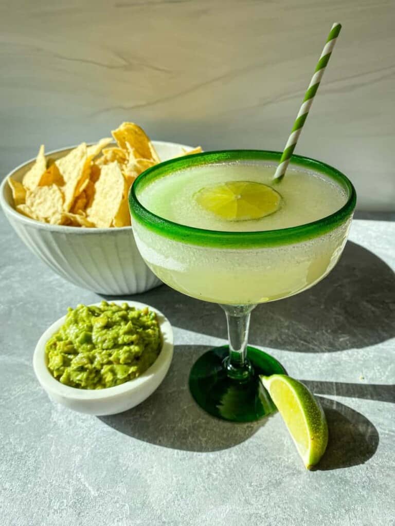 Frozen margarita with chips and guacamole on a table. Frozen Minute Maid Limeade Margarita in a margarita glass with a lime wedge.