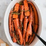 Long orange carrots with minced garlic and honey glaze in a baking dish.