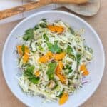 Vibrant side dish of a salad with herbs, fennel, and oranges slices on a white plate.