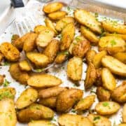 A tray of roasted potatoes sprinkled with fresh green herbs. A spatula is ready to serve with tilapia.