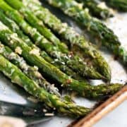 Bright green asparagus on a baking tray with melted shredded parmesan.