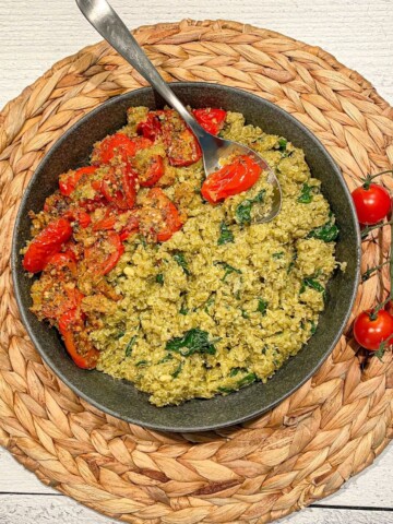 Quinoa with Pesto and Roasted Tomatoes in a bowl with a spoon and fresh tomatoes on the vine on the side.