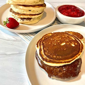 A stack of pancakes in the background and a pancake stuffed with nutella oozing out in the front with a strawberry.