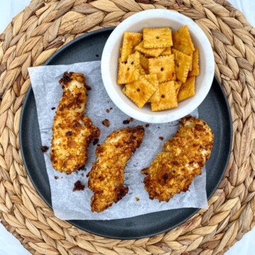 Air fryer Cheez-It Crusted Chicken Tenders on a plate with a bowl of Cheez-It crackers on the side.