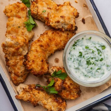 Cheez-It chicken tenders on a baking sheet with a small bowl of ranch dipping sauce.