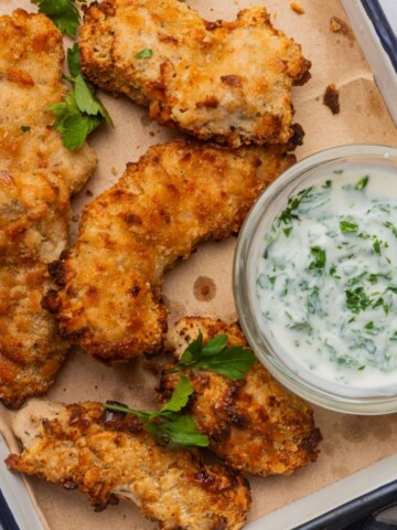 Cheez-It chicken tenders on a baking sheet with a small bowl of ranch dipping sauce.