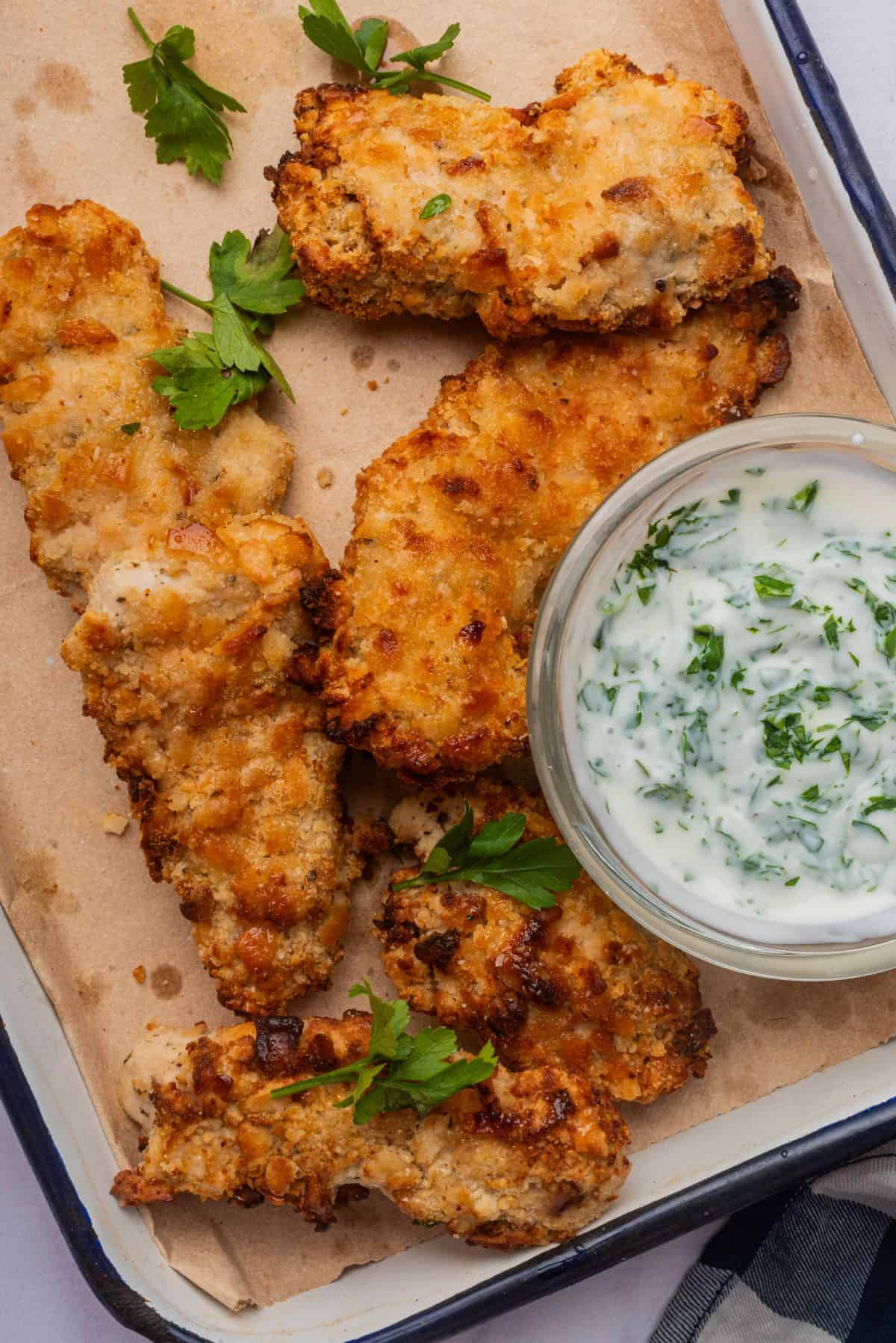 Cheez-It chicken tenders on a baking sheet with a small bowl of ranch dipping sauce.