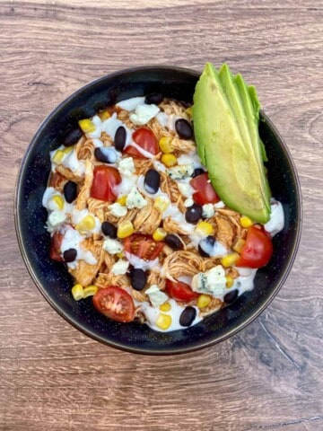Buffalo Chicken Bowl topped with black beans corn, tomatoes, avocado slices, ranch dressing, and blue cheese.