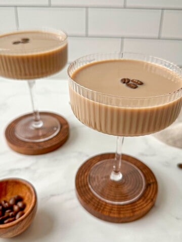 Two cold brew martinis garnished with coffee beans in coupe glasses.