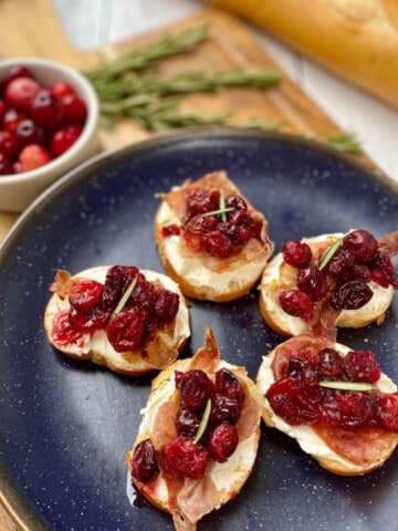 Cranberry, Prosciutto, and Whipped Goat Cheese Crostini on a cutting board.