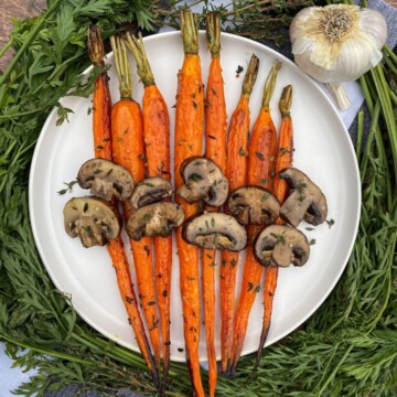 Roasted Garlic Carrots and Mushrooms on a white plate. A garnish for carrot tops, fronds.