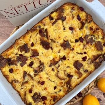 Cranberry orange panettone bread pudding with a bread box and lemons around the baking dish.