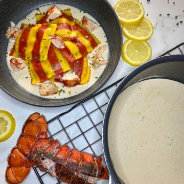A bowl of lobster ravioli with sherry cream sauce with a saucepan of sherry cream sauce and a lobster tail are on the side.