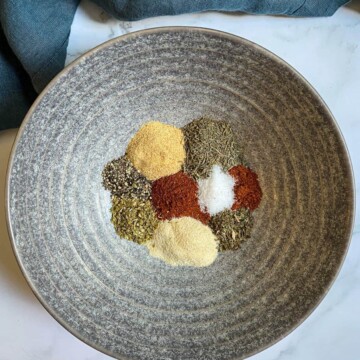 Spices used for blackened seasoning are separated in a gray bowl to show each individual spice color.