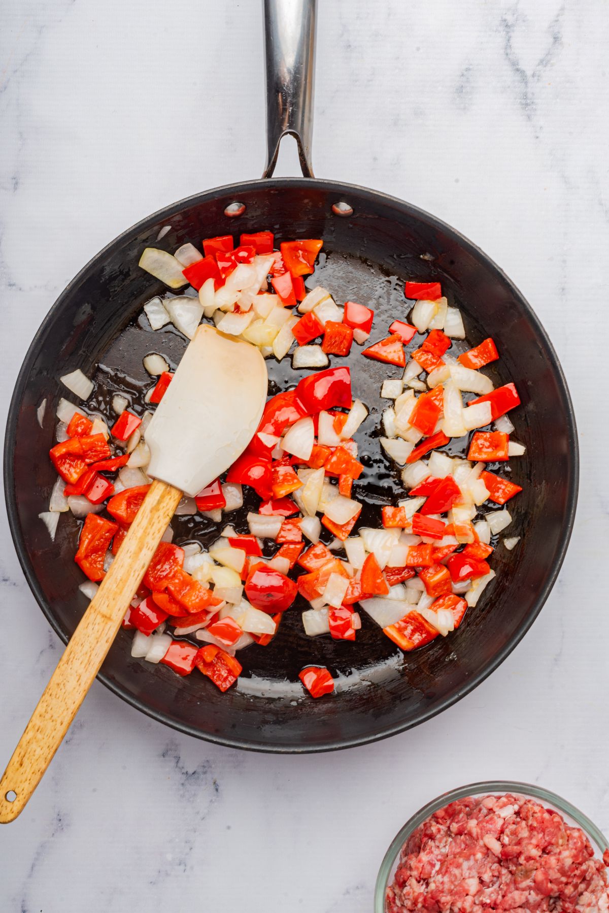 Chopped onions and red bell peppers sautéing in a skillet with a spatula.