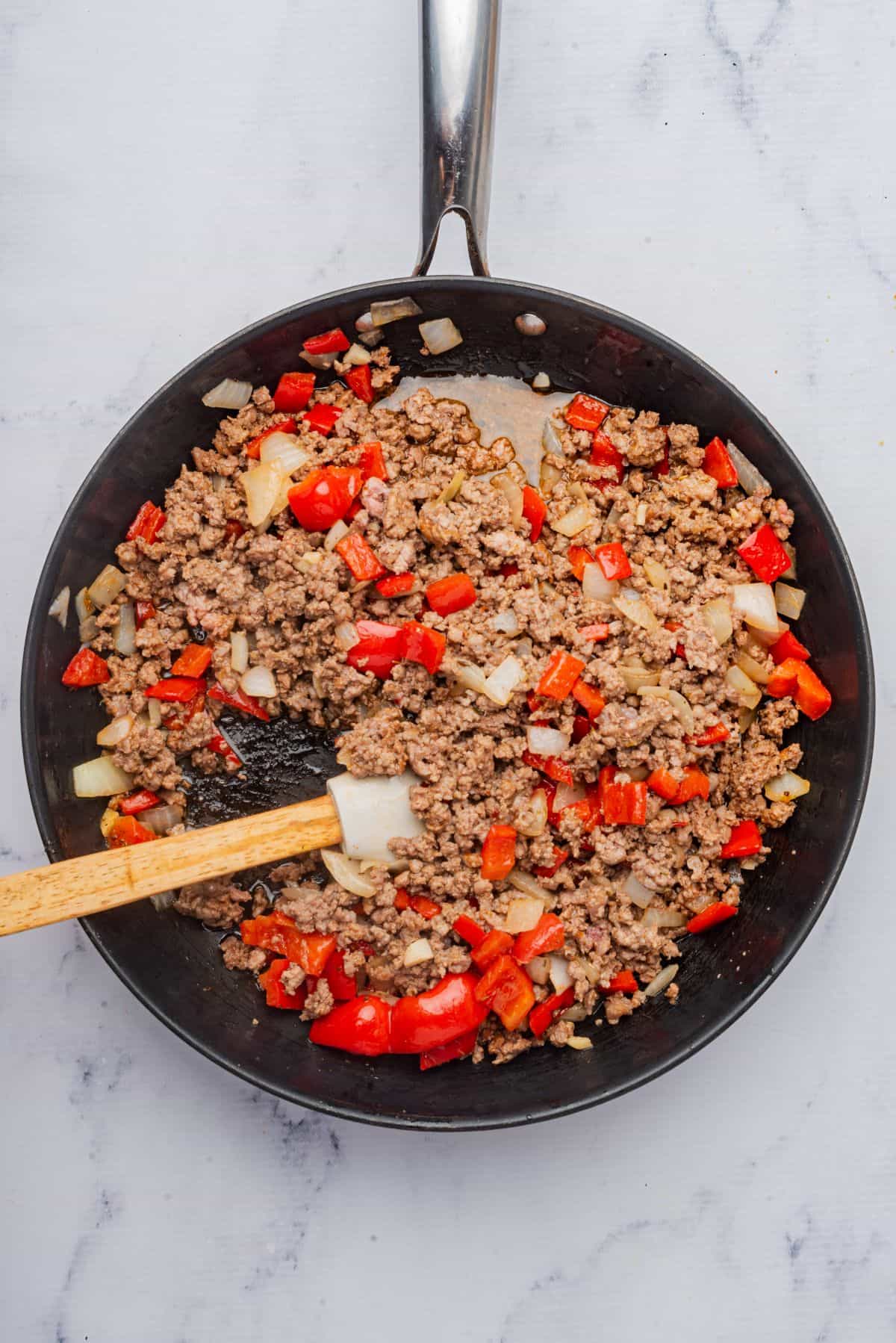 Ground beef, onions, and bell peppers cooking in a skillet with a spatula.