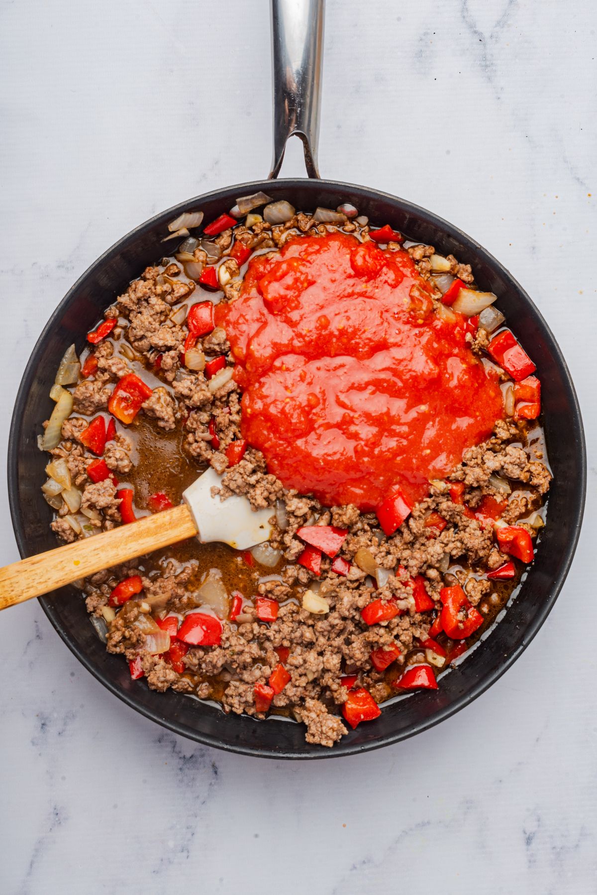 Tomato sauce and seasonings added to the skillet with a spatula.