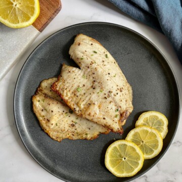 Frozen Tilapia Air Fryer recipe on a plate with lemon wedges on the side.