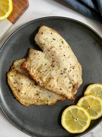 Frozen Tilapia Air Fryer recipe on a plate with lemon wedges on the side.