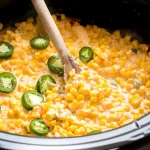Slow Cooker Cheesy Jalapeno Corn in a crockpot with a wooden spoon.