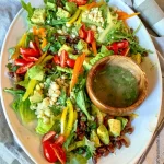 A fresh green cowboy salad with a side of vinaigrette dressing.