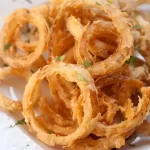 Crispy onion rings piled on a plate. A side for sloppy joes or sandwiches.