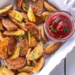 Crispy baked potato wedges are on a plate with a red dipping sauce.