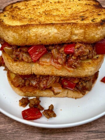 Sloppy joes on Texas toast stacked into a tall sandwich on a white plate.
