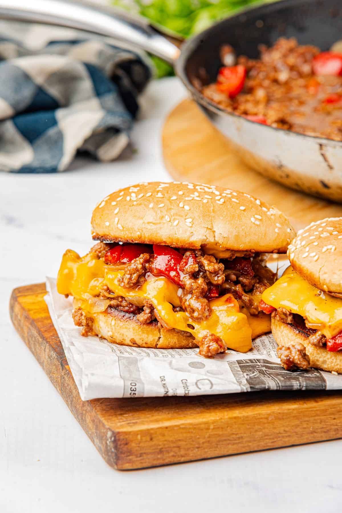 Sloppy Joes with cheese on a wooden cutting board with homemade sauce in a skillet.