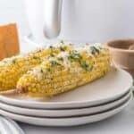 Two air fryer corn on the cob with parmesan and parsley garnish.