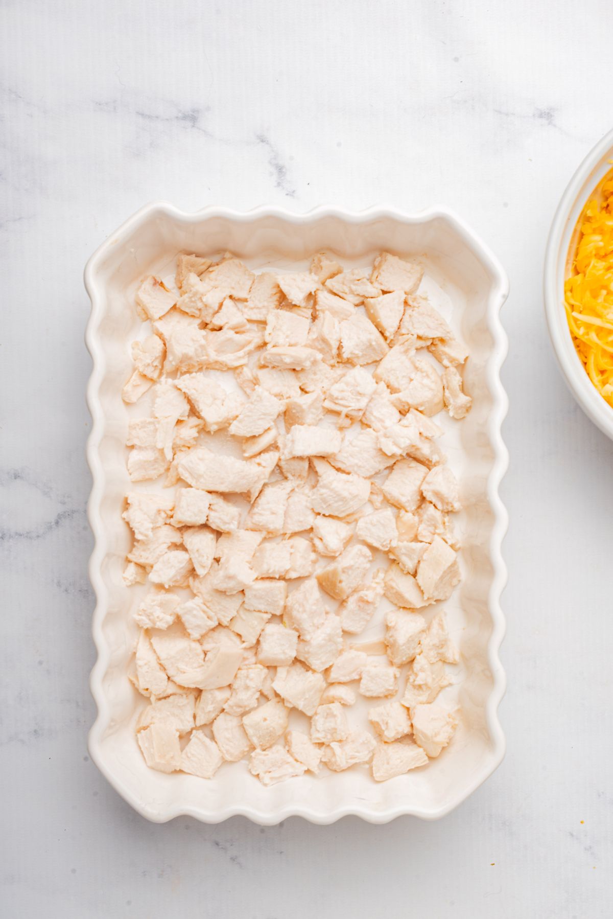 A layer of cooked diced chicken in a casserole dish.