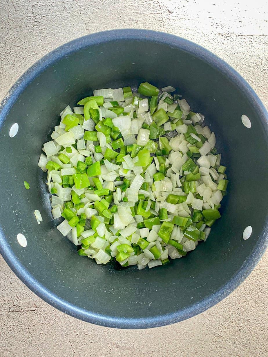 Onions, green bell pepper, and jalapeno are sautéing in a large pot.