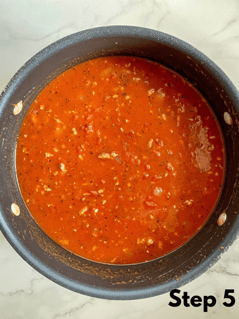 A Dutch oven with canned tomatoes newly added to the soup base of sausage, vegetables, and spices. 
