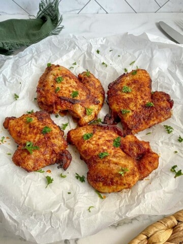 Boneless Skinless Chicken Thighs cooked in the air fryer are on parchment paper and sprinkled with fresh green parley.