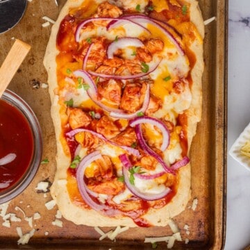 BBQ chicken flatbread on a baking tray with a bowl of bbq sauce on the side.