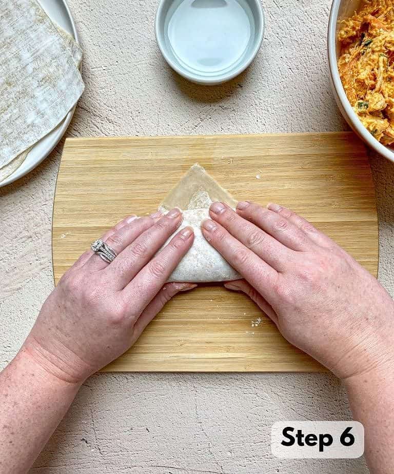 Hands shown rolling a buffalo chicken egg roll tightly from bottom to top.