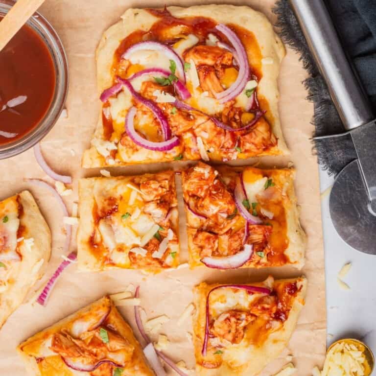 BBQ chicken flatbread pizza on a cutting board sliced into six square pieces.