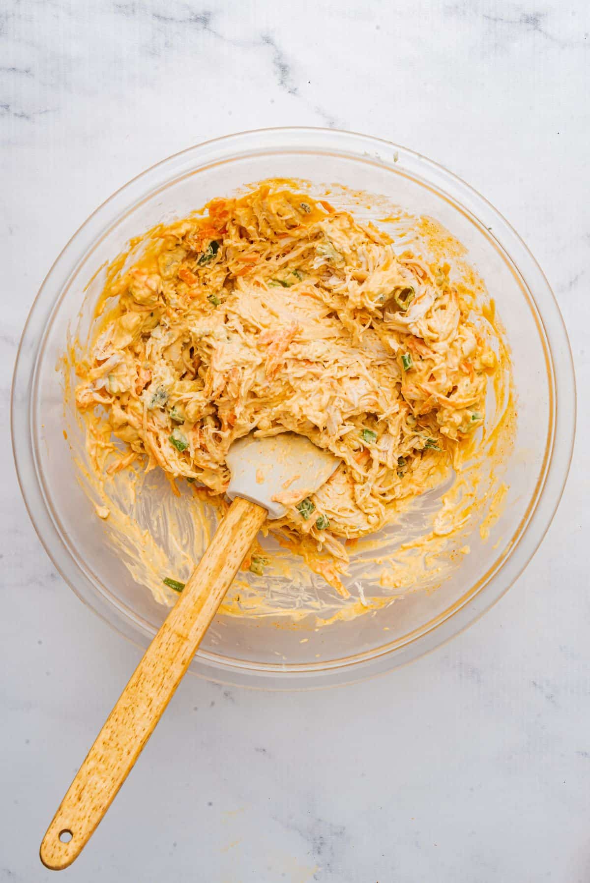 Buffalo chicken filling mixed in a large bowl with a spatula.