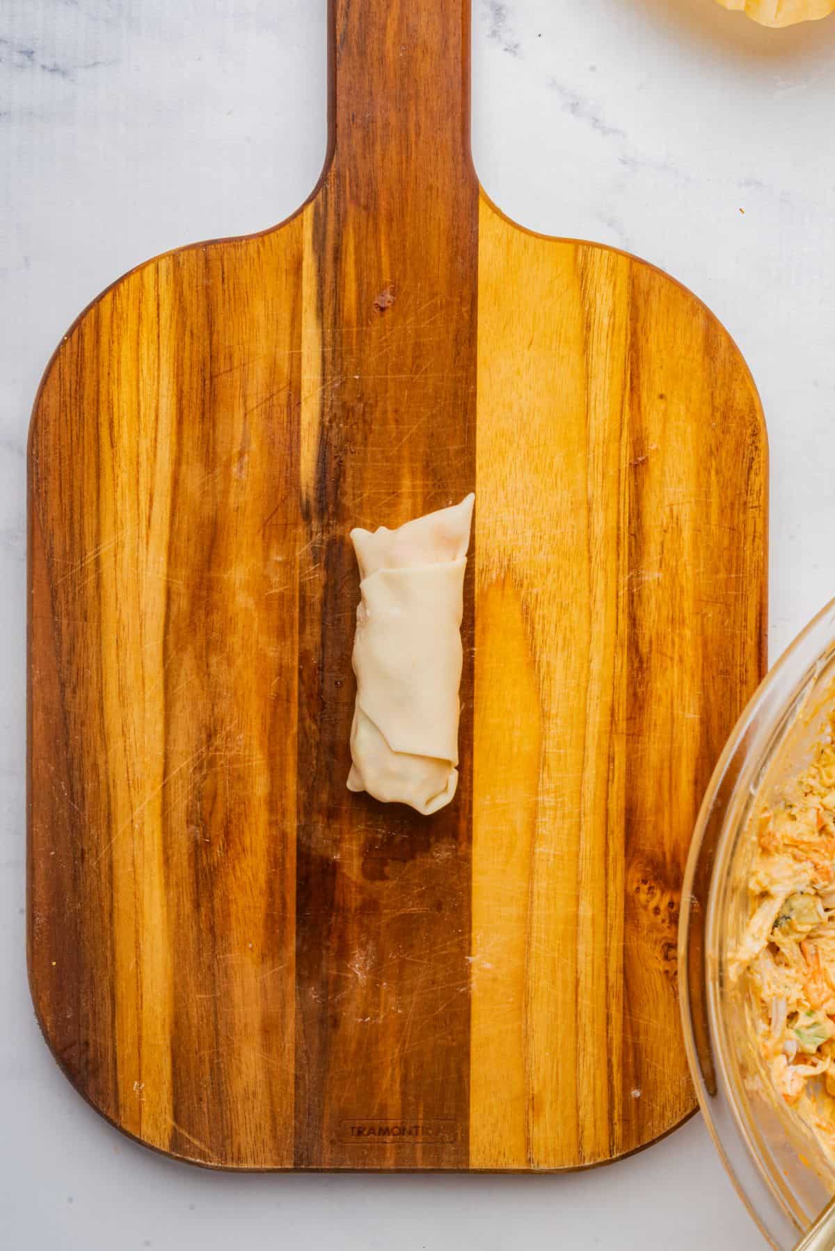 Egg roll tightly wrapped on a wooden cutting board.