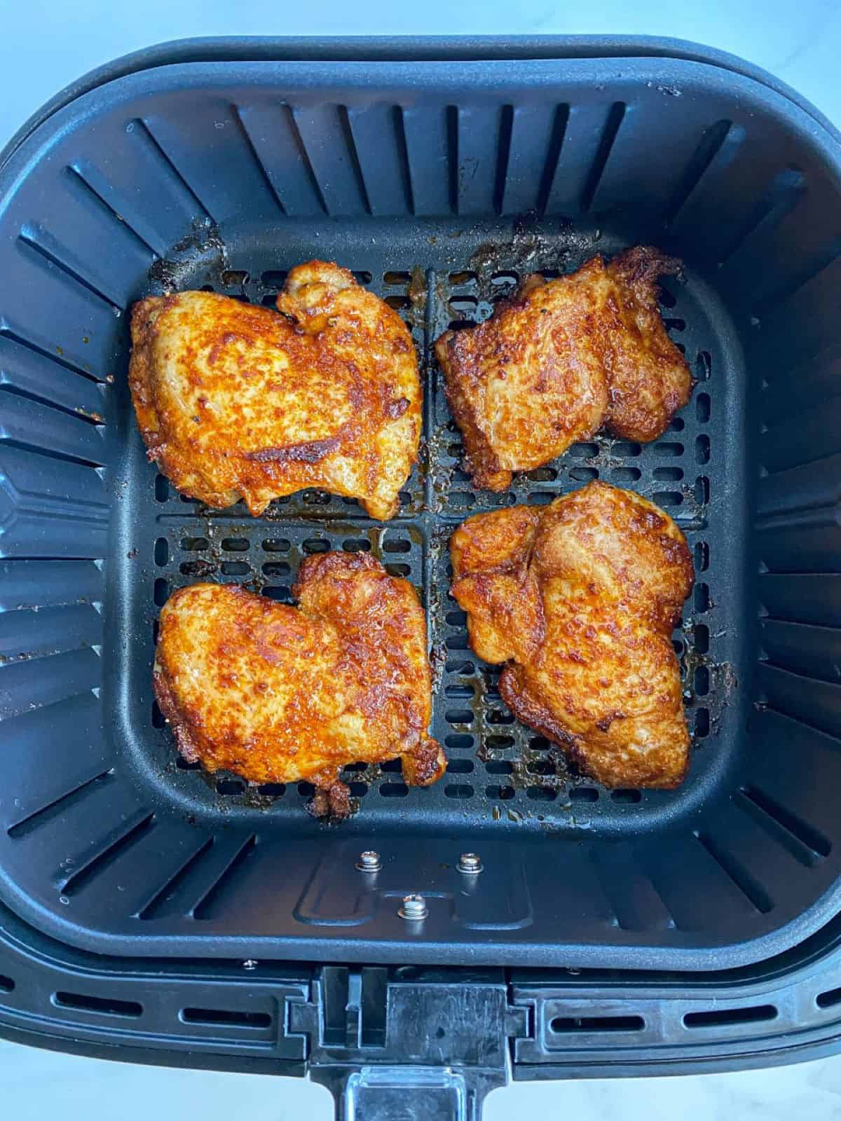 Cooked air fryer chicken thighs in an air fryer basket.