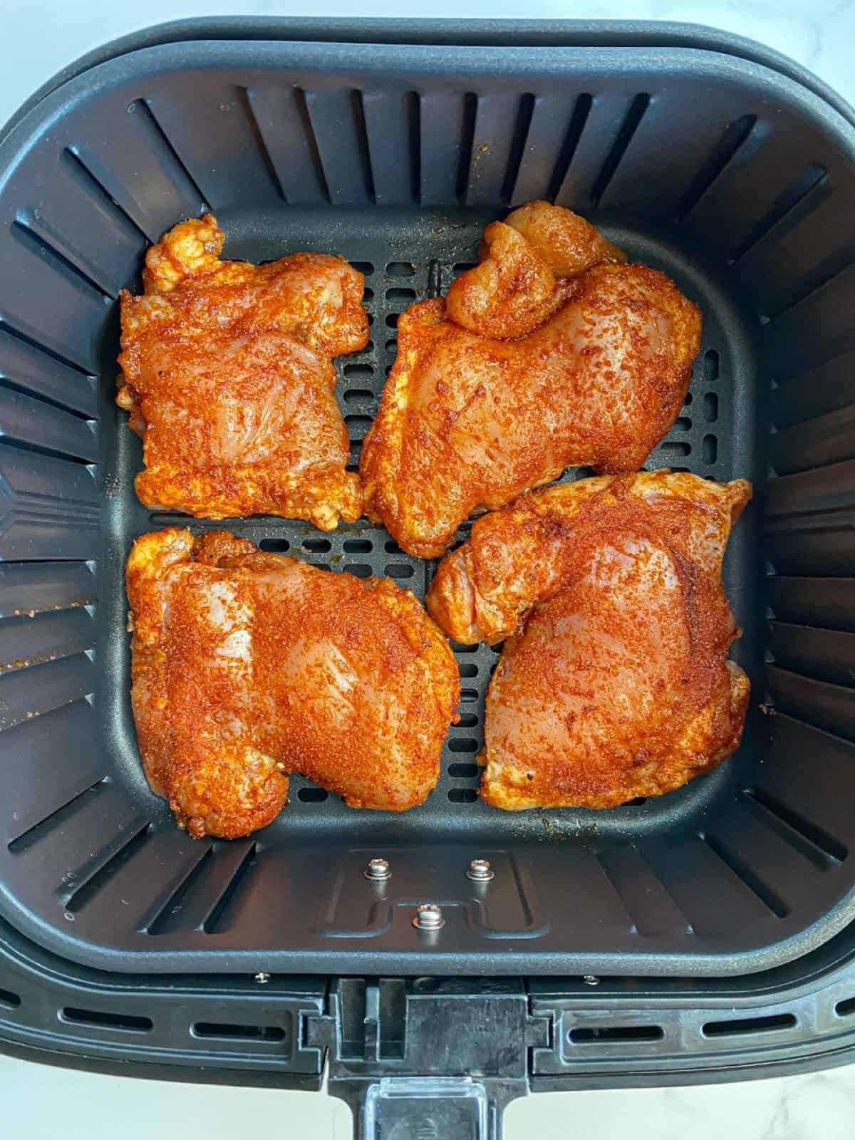 Uncooked chicken thighs in air fryer basket.
