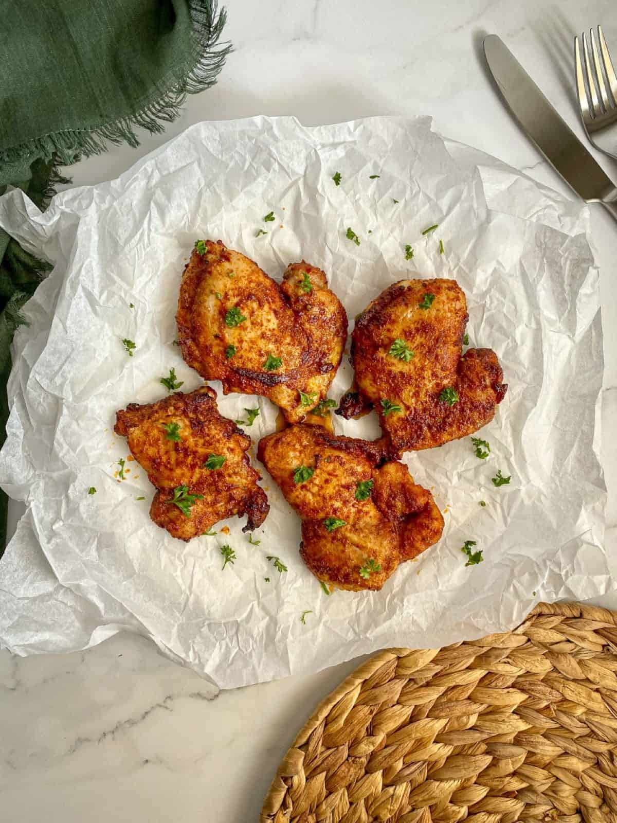 Air Fryer chicken thighs on parchment paper with fresh parsley sprinkled on top.