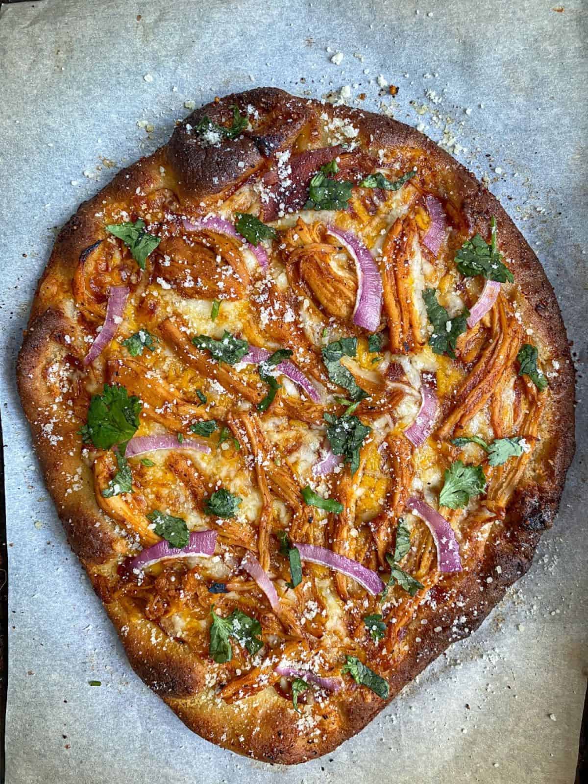 Naan pizza with BBQ chicken, cheese, red onion, and cilantro on parchment paper.