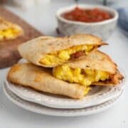 A breakfast quesadilla filled with eggs and bacon is on a plate with salsa in a bowl.
