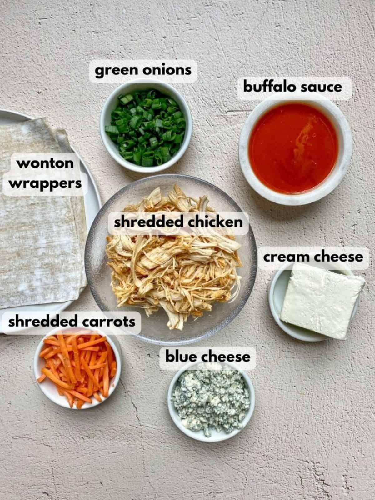 Ingredients needed for buffalo egg rolls: shredded chicken, egg roll wrappers, cream cheese, blue cheese, carrots, buffalo sauce, and green onions.