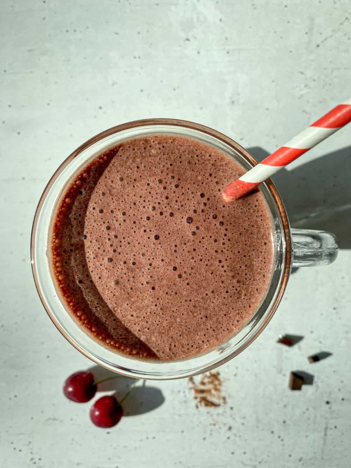 An overhead image of a creamy chocolate cherry smoothie with a red and white straw.