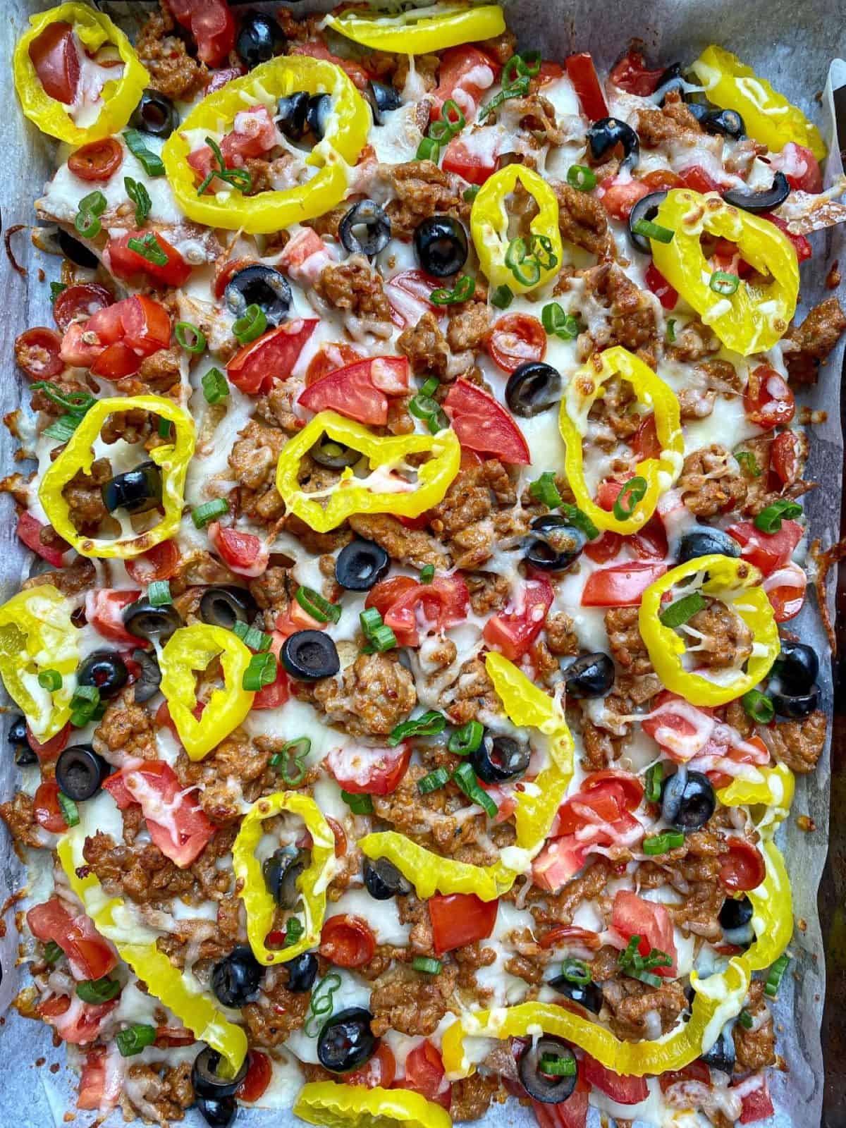 Baked Nachos on a sheet pan loaded with sausage, cheese, and vegetables.
